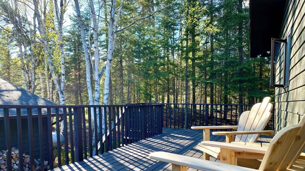 A wooden deck with Adirondack chairs, surrounded by a forest. - Cheerful Lutsen getaway 4bdrms and wifi (Lutsen)