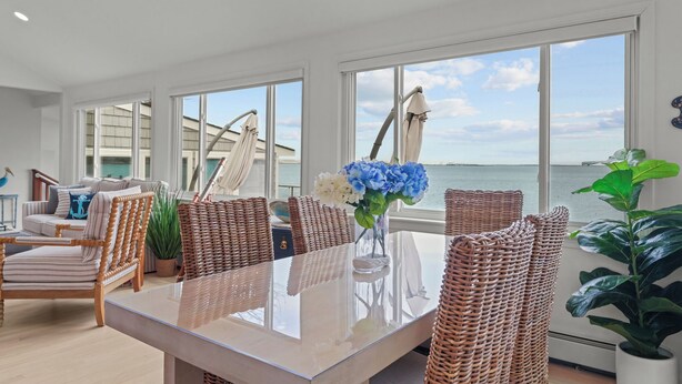 A dining area with a glass table, wicker chairs, and a view of the sea. - Luxury seaside retreat (North Kingstown)