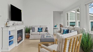 A modern living room with a fireplace, striped sofas, a television, and large windows. - Luxury seaside retreat (North Kingstown)