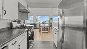A modern kitchen with white cabinets, stainless steel appliances, and a dining area with a view of the ocean. - Luxury seaside retreat (North Kingstown)