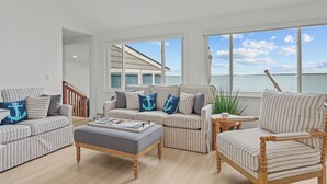 A spacious living room with striped furniture, a wooden coffee table, and large windows offering a view of the sea. - Luxury seaside retreat (North Kingstown)