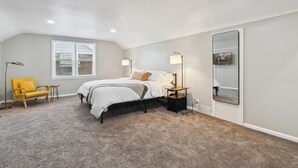 A bedroom with a bed, a nightstand, a lamp, a chair, a window, and a mirror. - Plainview Haven (Detroit)