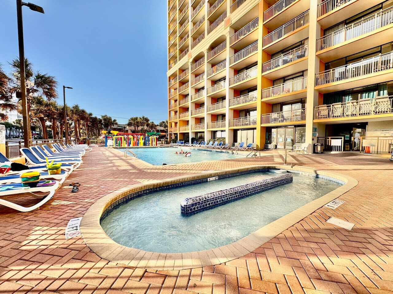A hotel with a swimming pool, lounge chairs, and a multi-story building with balconies.