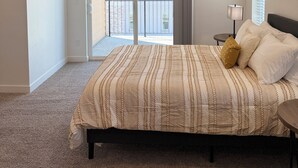 A bedroom with a large bed, a nightstand, a lamp, and a view of the outside balcony. - Brand New Condo in Spanish Fork (Spanish Fork)