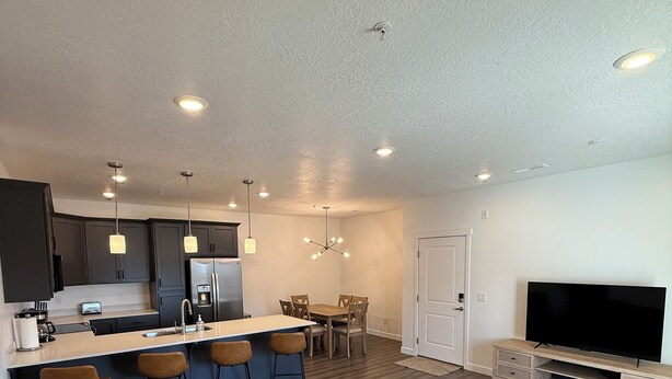 A modern living room with a sofa, a TV, and a kitchen area with bar stools. - Brand New Condo in Spanish Fork (Spanish Fork)