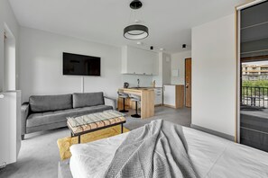 Un salón moderno y minimalista con un sofá gris, una mesa de centro de vidrio y una cama con manta gris.