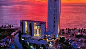 A high-rise hotel with multiple floors, a swimming pool, and a beach area with palm trees. - Charming Oceanfront Condo (Puerto Vallarta)