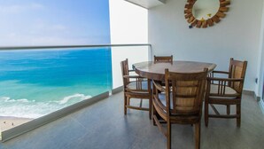 A balcony with a round wooden table and chairs, overlooking a beach with turquoise water. - Charming Oceanfront Condo (Puerto Vallarta)