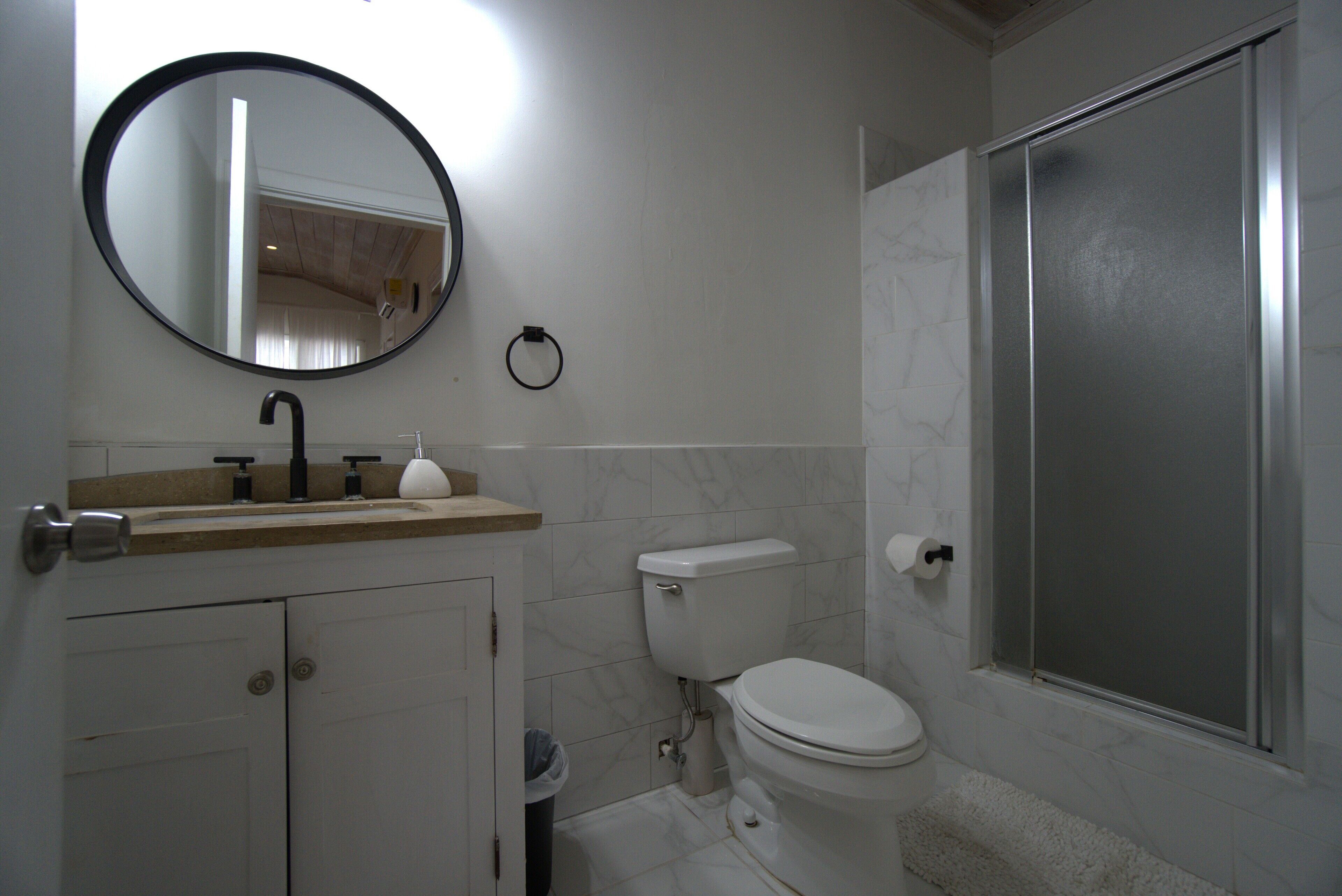 A bathroom with a toilet, sink, mirror, and shower.