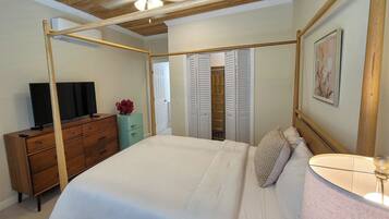 Un dormitorio con cama con dosel, ventilador de techo, televisor sobre un aparador de madera y armario con puertas correderas.