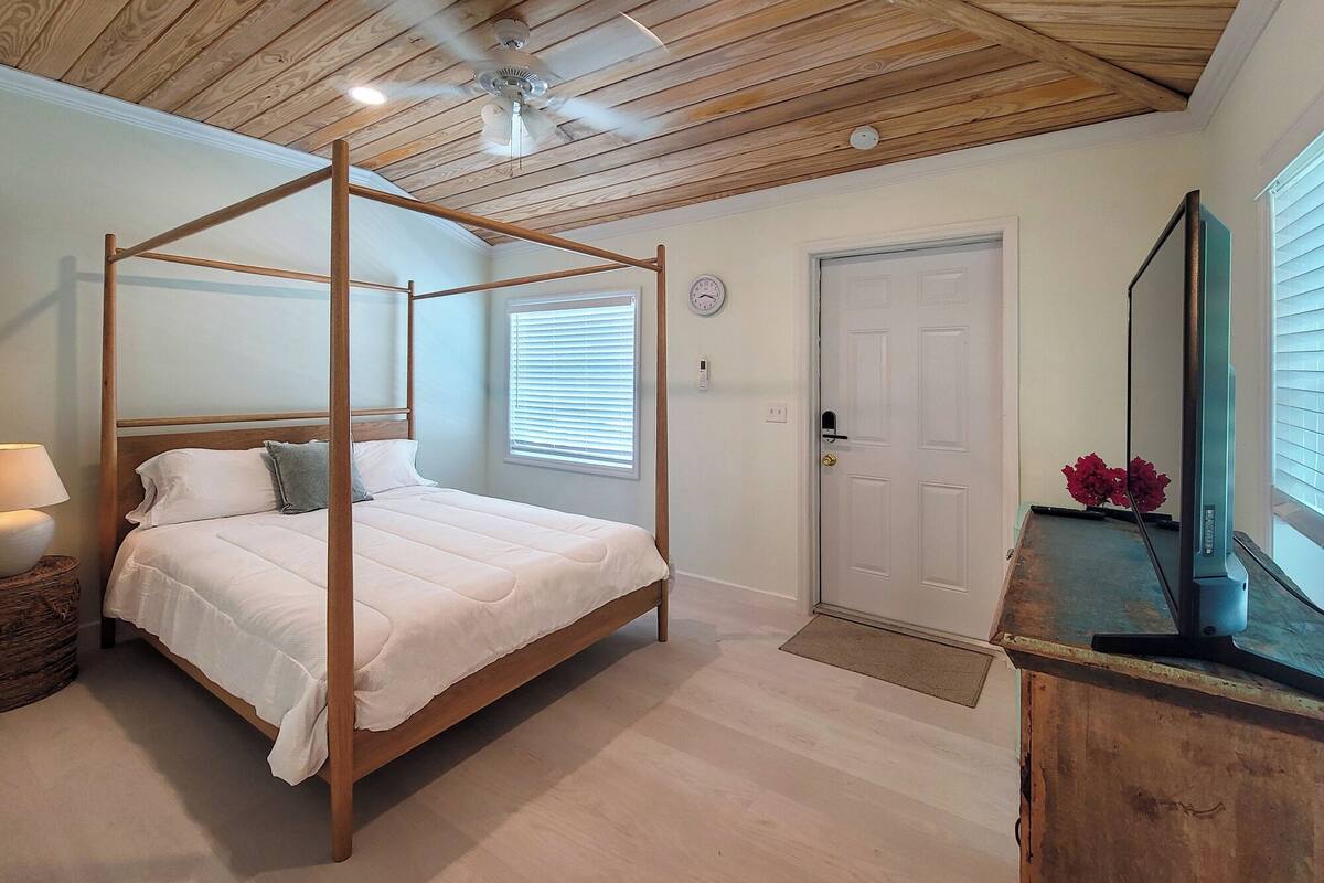 Ein Schlafzimmer mit einem Himmelbett, einem Deckenventilator, einer Uhr und einer Tür.