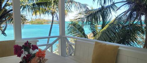 Ein Zimmer mit Blick auf das Meer, ein weißer Tisch mit Blumen in einer Vase und ein weißes Geländer.