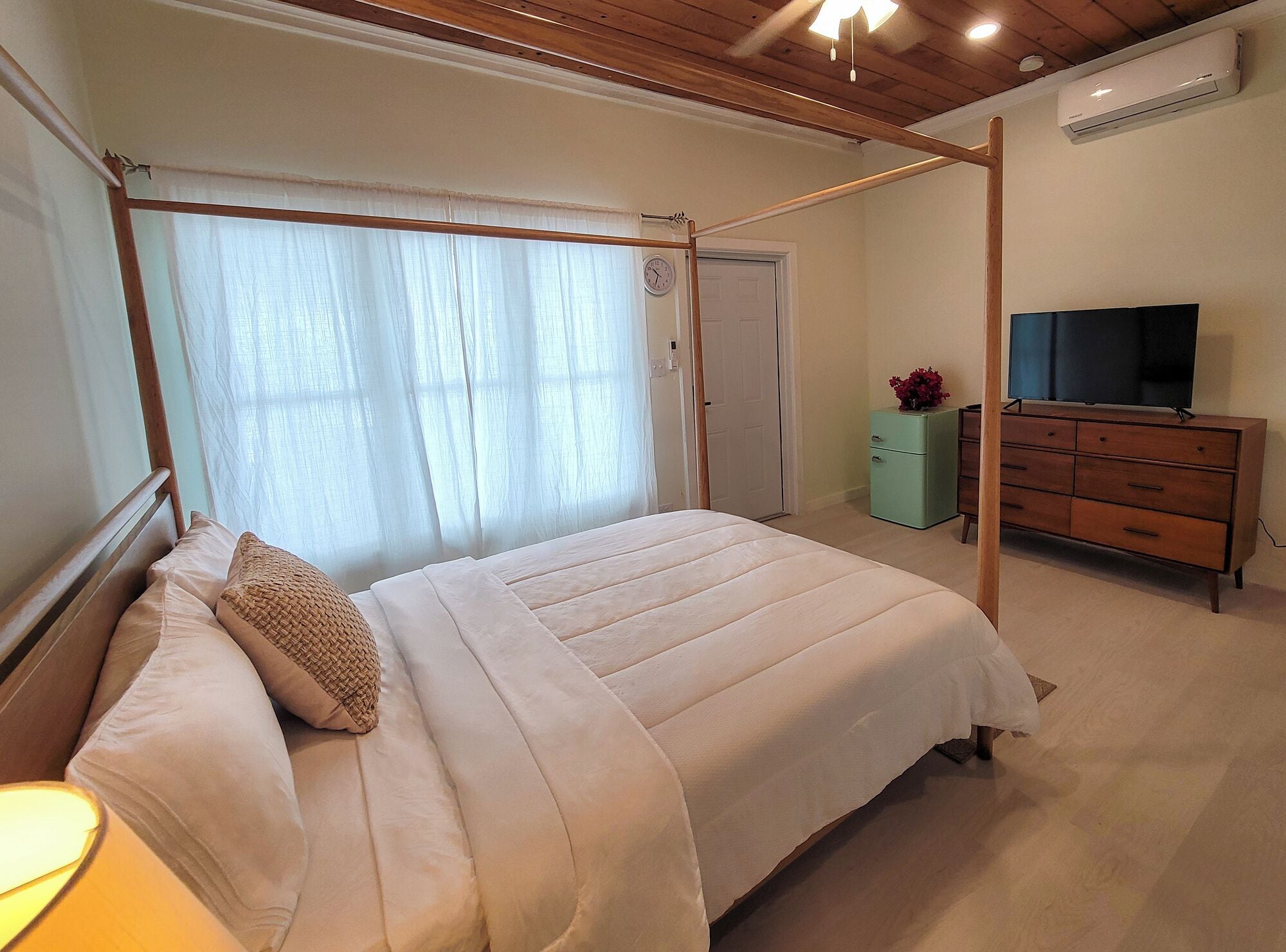 A bedroom with a bed, a dresser, a television, and a window with curtains.