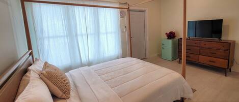 A bedroom with a bed, a dresser, a television, and a window with curtains.