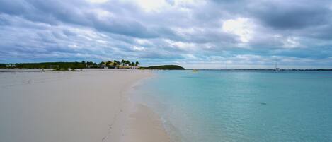 Une plage à l’eau turquoise et limpide, un rivage sablonneux et une île qui se dessine à l’horizon.