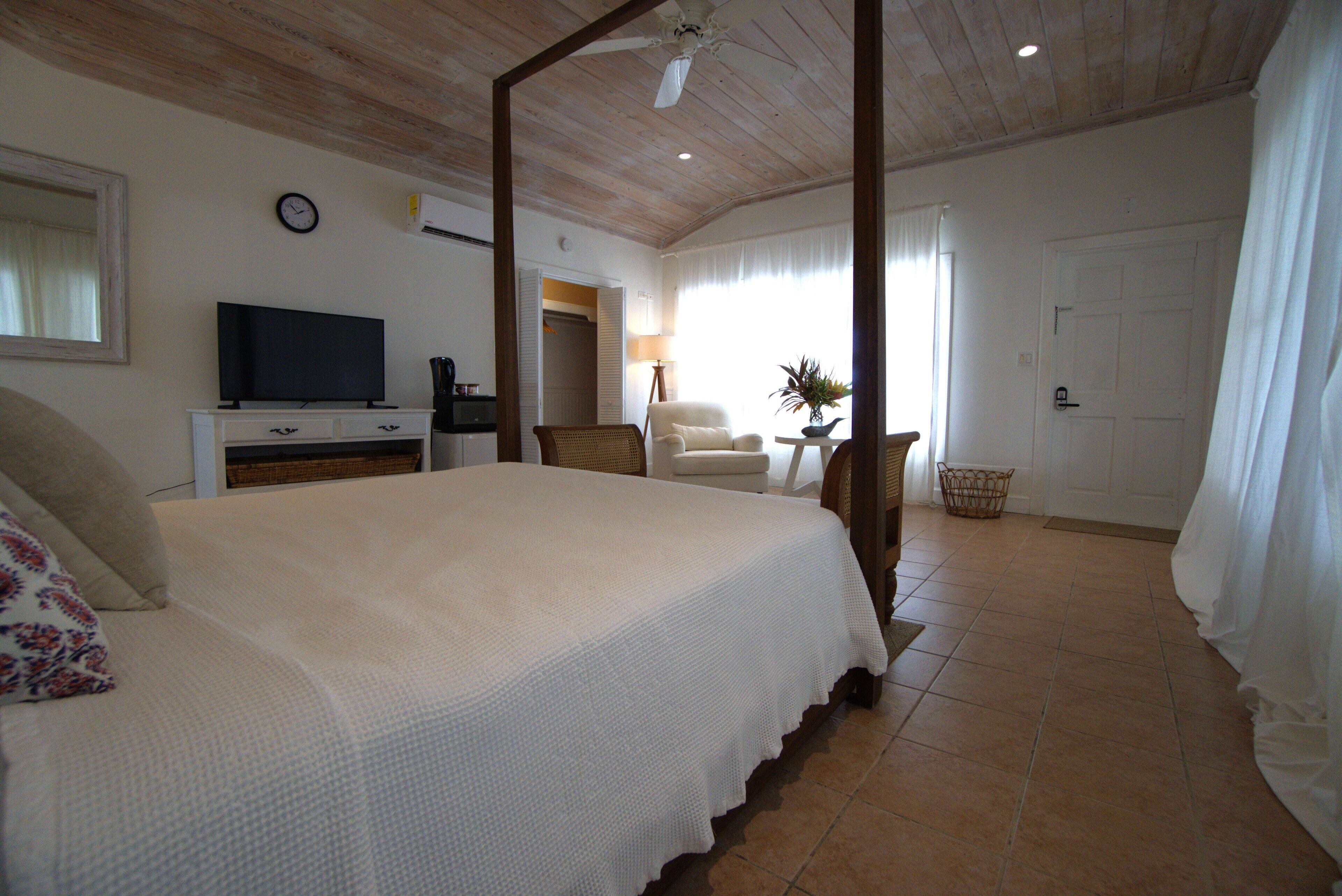 A spacious bedroom with a large bed, a television, a wardrobe, and a bathroom visible through an open door.