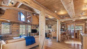Ein rustikales Blockhaus-Interieur mit großem Fenster, Holzböden, einer Couch und einem Essbereich.