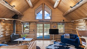 Ein rustikales Blockhaus-Interieur mit Kamin, Fernseher, einer Couch und einem großen Fenster.
