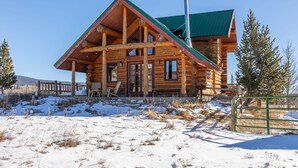 Eine Blockhütte mit grünem Dach, Holzfassade und einer Veranda mit Stühlen.