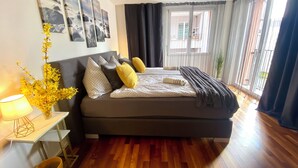 A modern bedroom with a large bed, a bedside table with a lamp, and a view of the outside through a window. - City Views & Comfort at Schaffhauserplatz (Zürich)