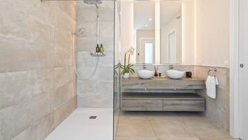 Un baño moderno con ducha envuelta en vidrio, tocador de madera con lavabo blanco y un espejo grande.