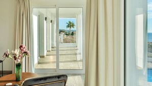 Ett hotellrum med ett stort fönster, utsikt över en palm och en pool, och en vas med blommor på ett bord.