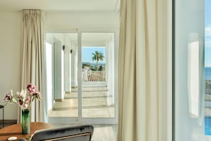 A hotel room with a large window, a view of a palm tree and a pool, and a vase with flowers on a table.
