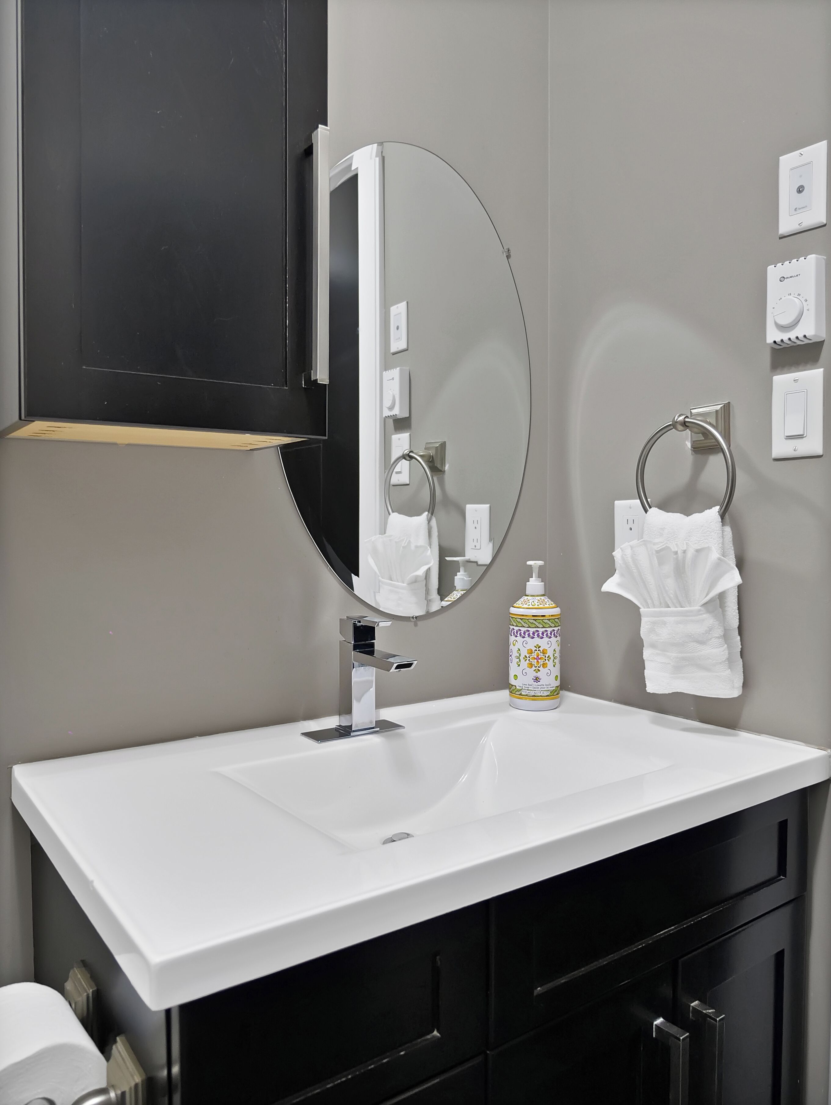 A modern bathroom with a white sink, a large mirror, a towel rack, and a bottle of hand soap.