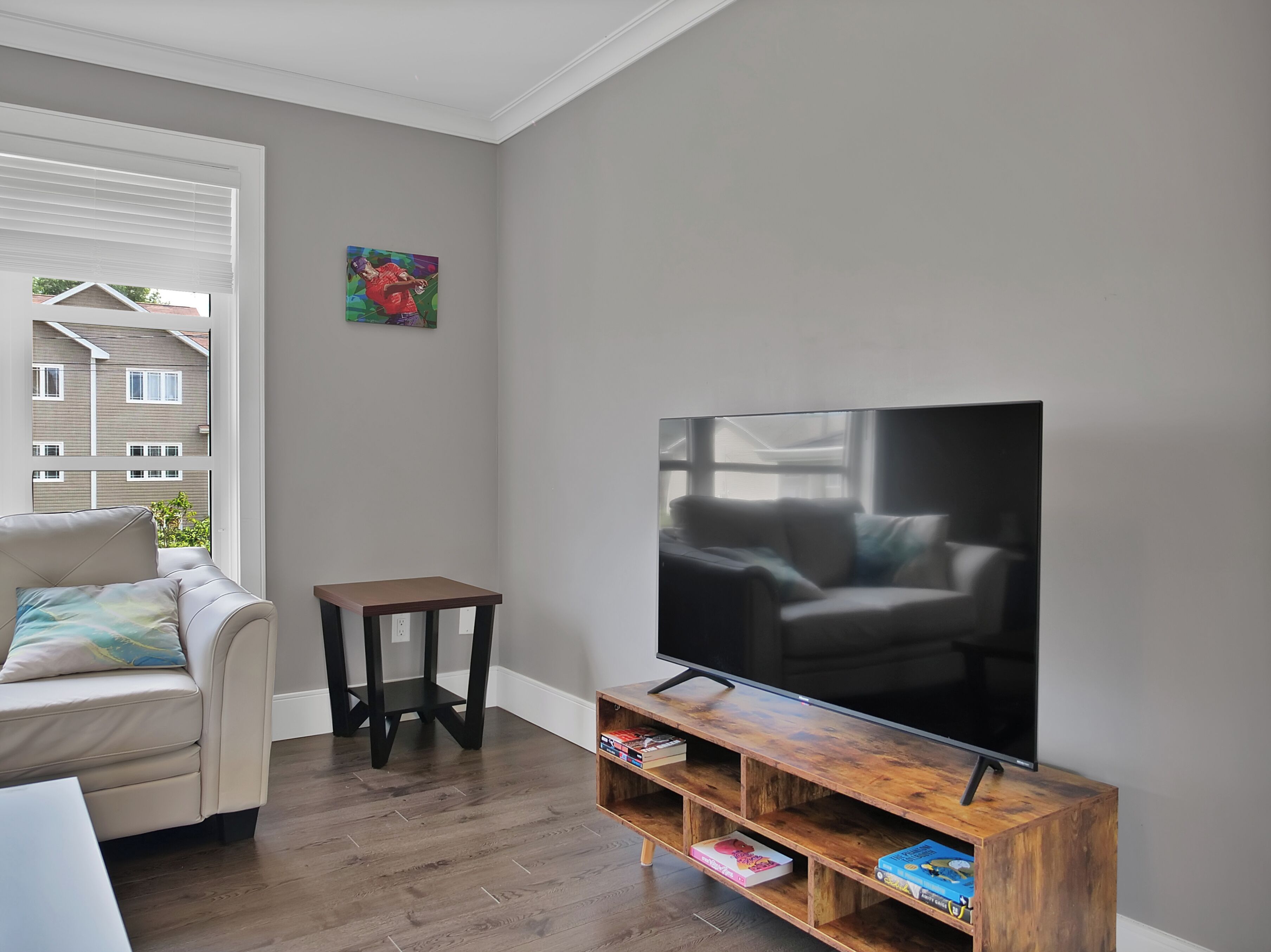Un salon avec un grand téléviseur à écran plat posé sur un meuble en bois, un canapé beige et une petite table.