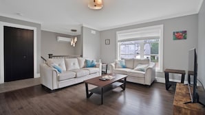 A modern living room with two white sofas, a wooden coffee table, and a TV stand.