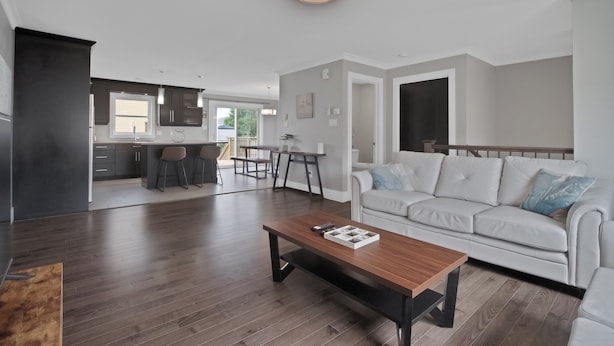 A modern living room with a wooden coffee table, a white sofa, and a kitchen in the background.