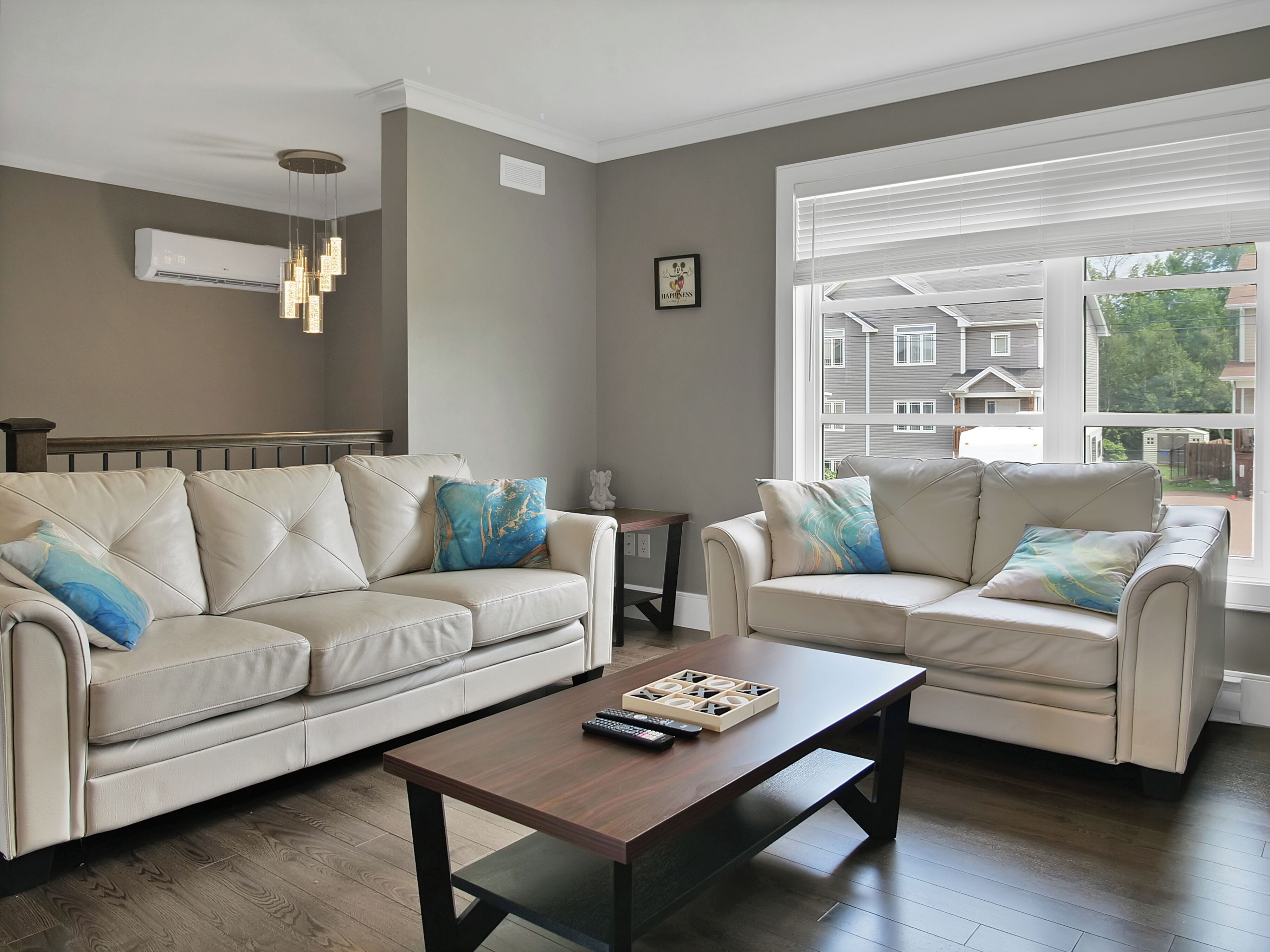 Un salón con dos sofás de cuero color beige, una mesa de centro de madera y vistas a edificios residenciales a través de amplios ventanales.
