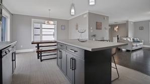 A modern kitchen with a central island, pendant lighting, and a dining area with a sofa.