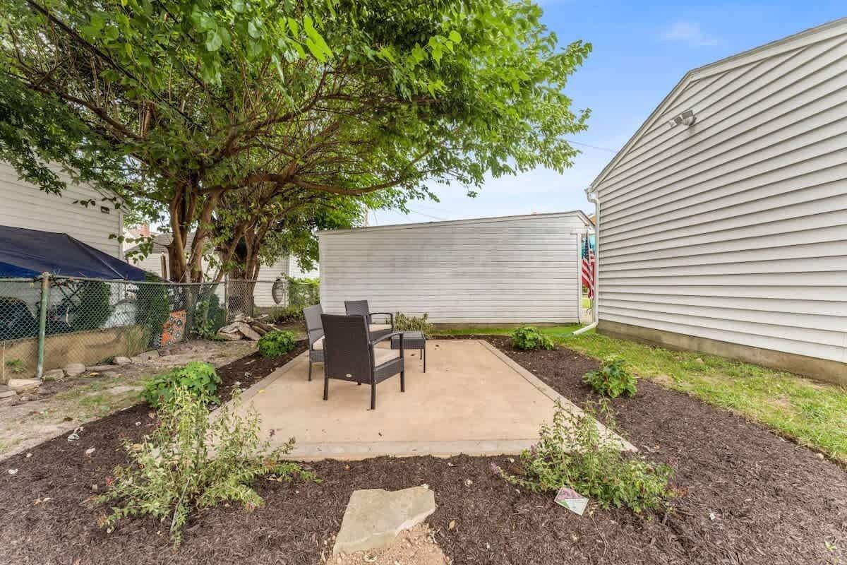 A patio area with a concrete floor, surrounded by a garden with mulch and small plants. There are two chairs and a table.