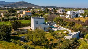 En moderne villa med swimmingpool, omgivet af frodig vegetation og et bakket landskab.