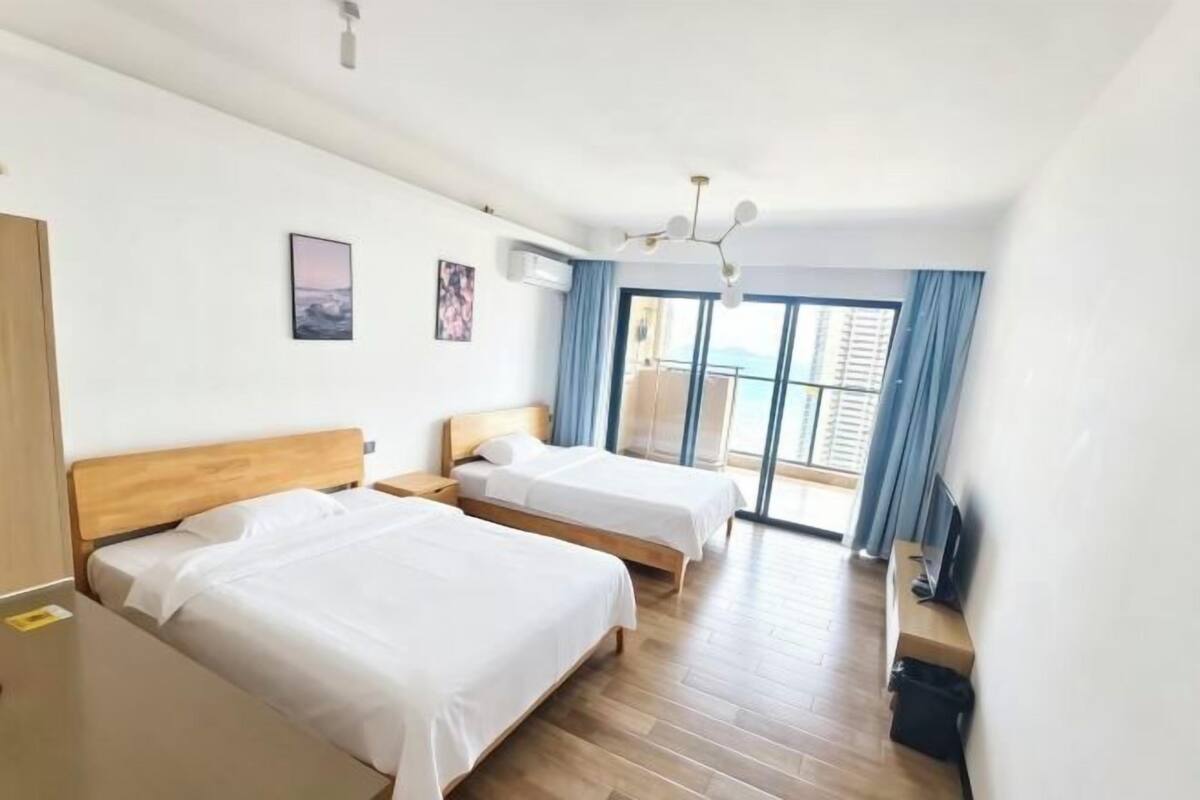 A hotel room with two beds, a TV, a desk, and a balcony with a view.
