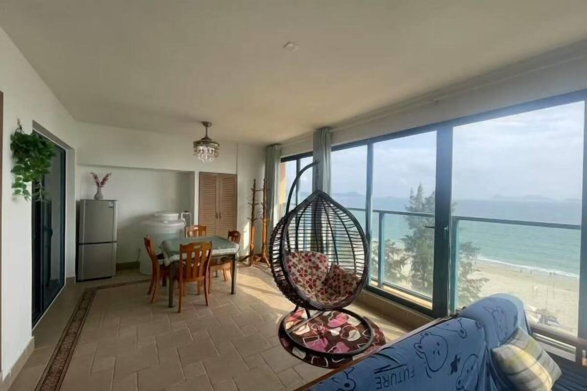 A balcony with a hanging chair, a dining area with chairs and a table, and a view of the sea.