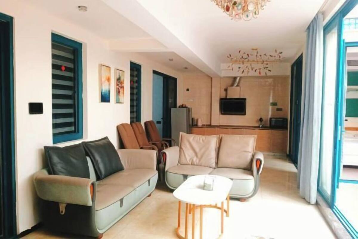 A living room with two sofas, a coffee table, and a TV. There is a kitchen area in the background.
