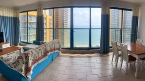 A corner room with a bed, a dining table, and a view of tall buildings and the sea. - Huidong Vanke Shuangyue Bay Xinyue Vacation Apartment (Huidong)