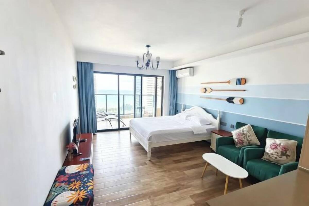 A hotel room with a bed, a green sofa, a small table, and a view of the city through large windows.