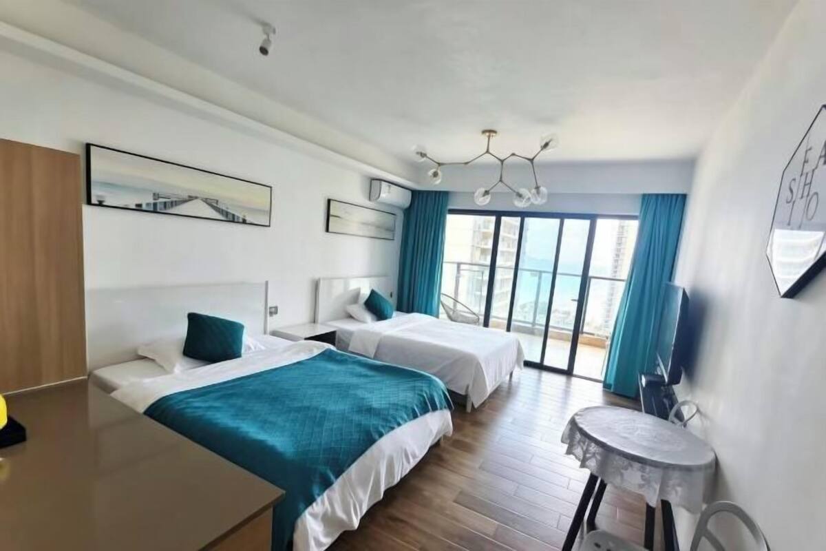 A hotel room with two beds, a desk, a chair, a small table, a TV, and a large window with curtains.