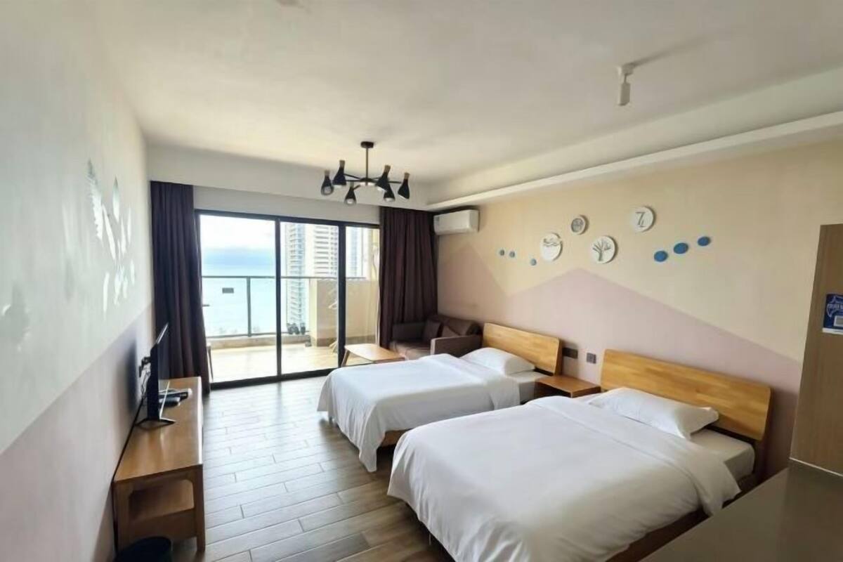 A hotel room with two beds, a desk, a chair, a TV, a chandelier, and a balcony with a view.
