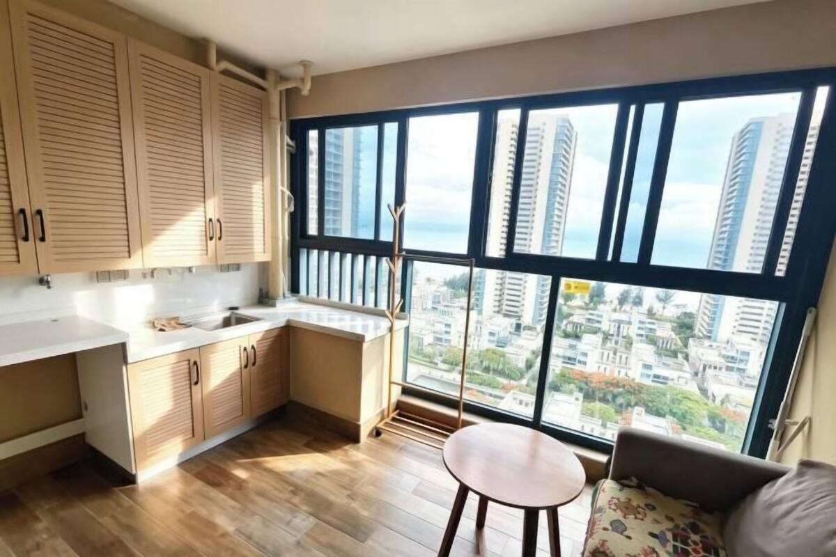 A modern kitchen with wooden cabinets, a sink, and a large window offering a city view.