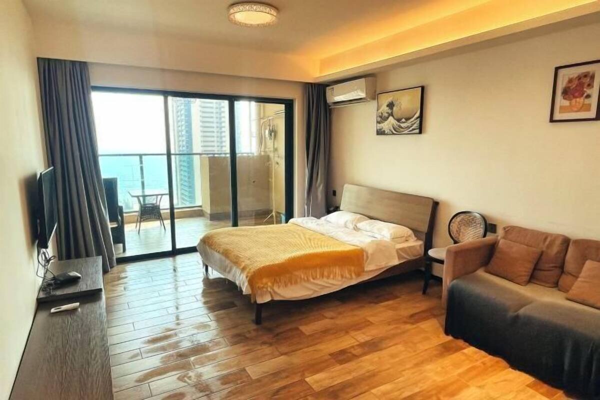 A hotel room with a bed, a sofa, a TV, and a balcony with a view.