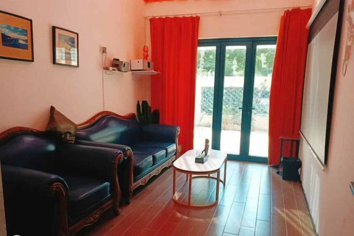 A living room with a dark blue sofa, a small round table, and a sliding glass door leading to an outdoor area.