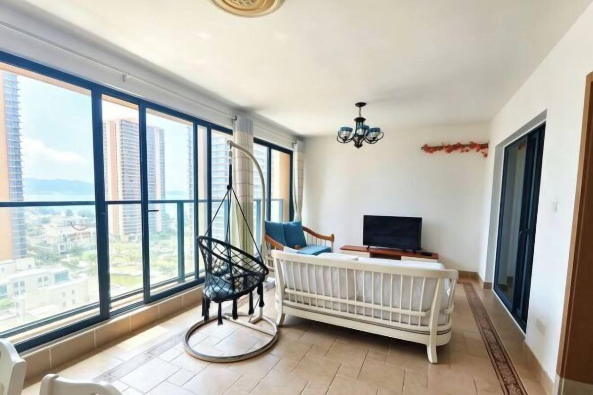 A spacious room with large windows, a hanging chair, a white sofa, and a TV.