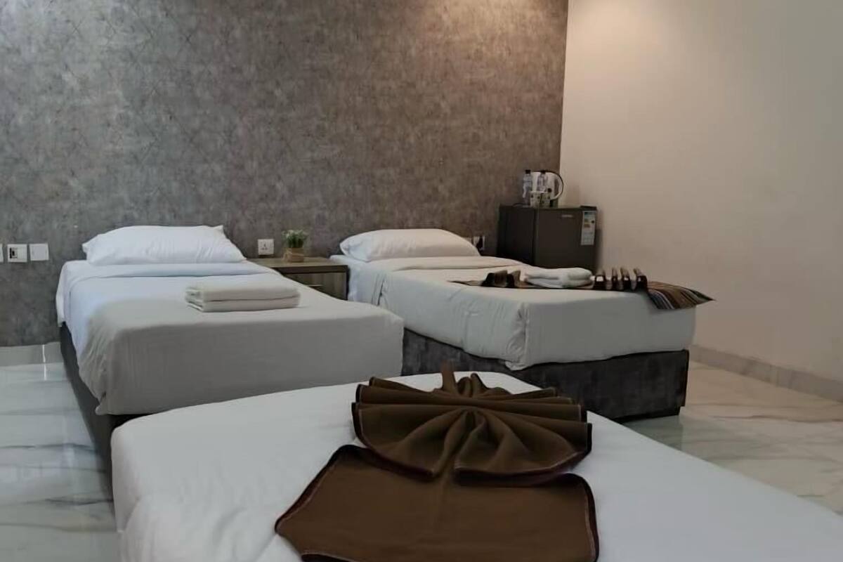 A hotel room with three beds, a marble floor, a grey textured wall, and a hanging light fixture.