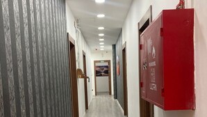 A hallway with patterned wallpaper, a red fire safety box, and a door at the end. - Gate inn hotel (Amman)