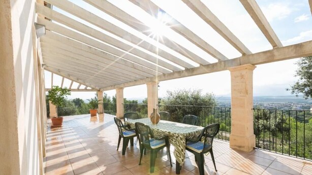 A covered outdoor patio with a table and chairs, overlooking a scenic landscape.