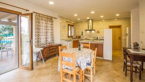 A modern kitchen with a central island, a dining area with a table and chairs, and a sliding glass door leading to an outdoor area.